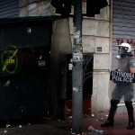 A protester armed with a hammer awaits for riot police officers behind a corner in Athens
